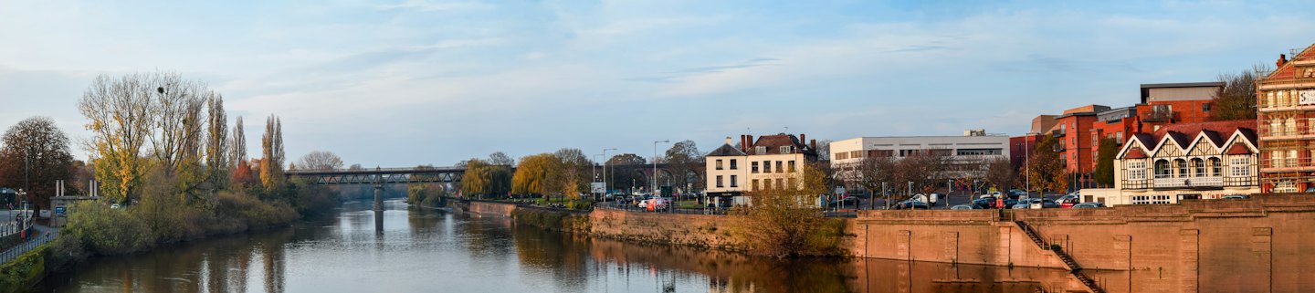 A metal bridge spans a river flowing through an urban area.