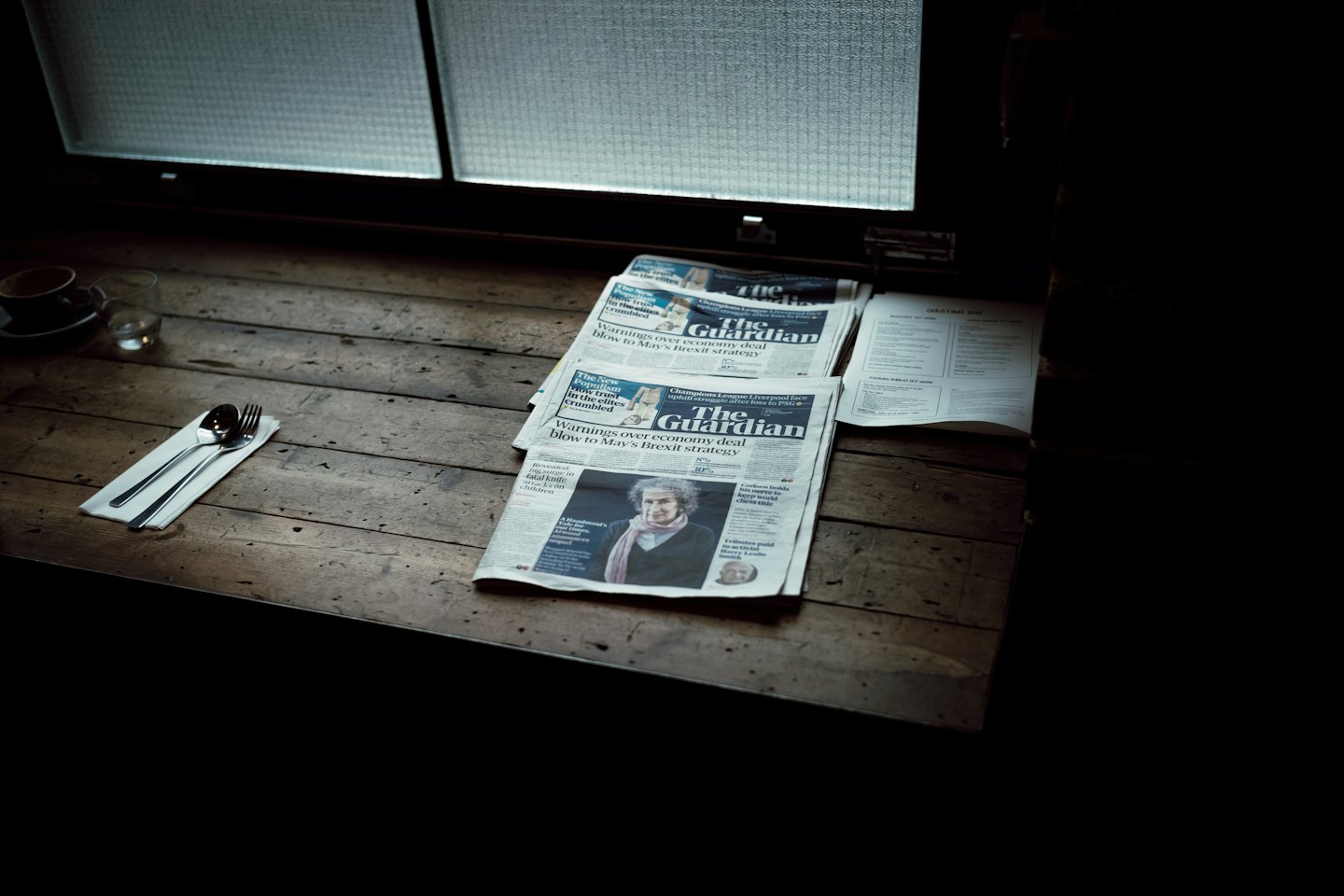 Stack of newspapers with coffee and cutlery on a wooden table.