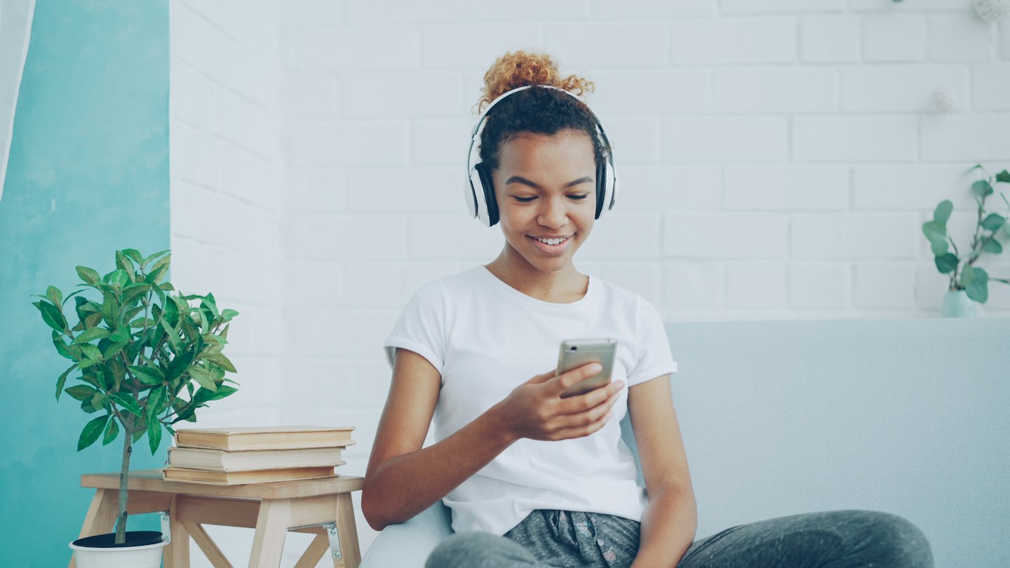 Woman wearing headphones smiles while looking at her smartphone.
