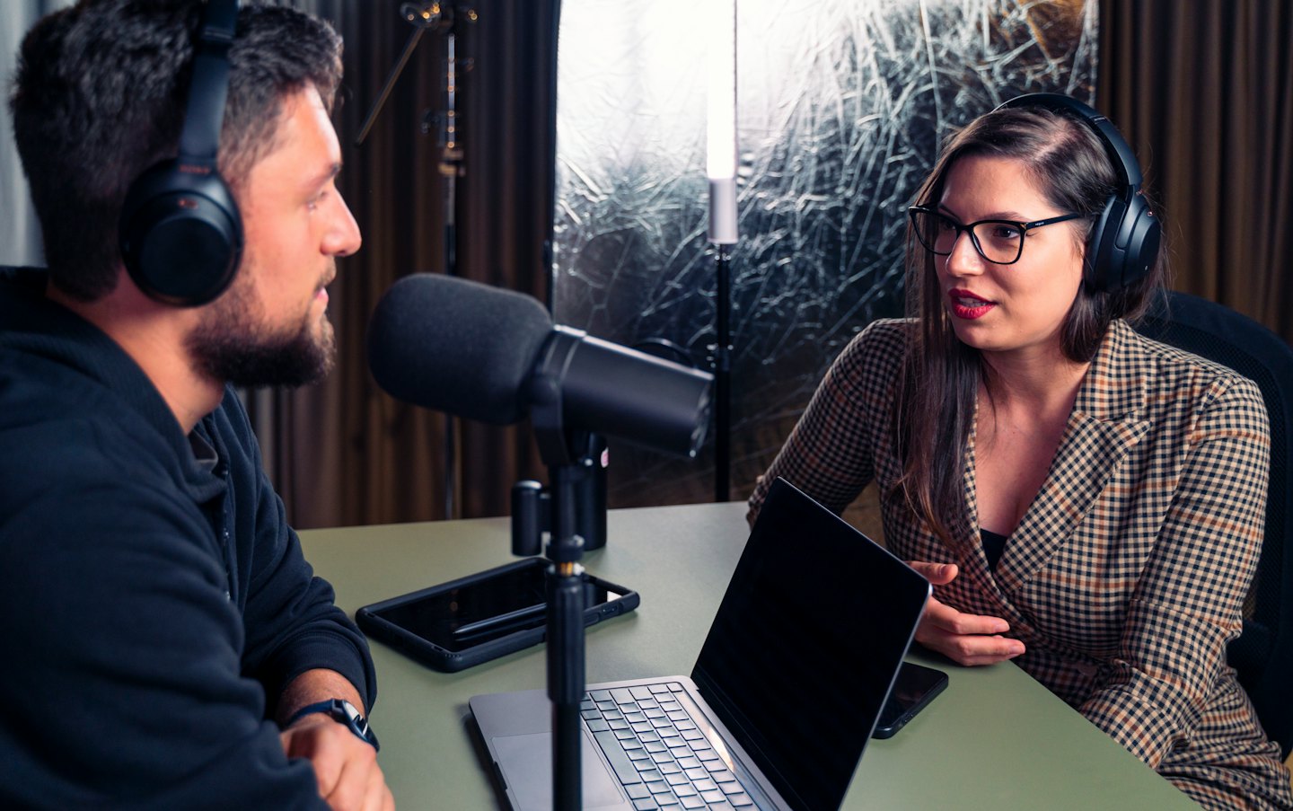 Two people wearing headphones record a podcast in a studio.